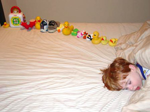 boy sleeping in a bed with ducks and toys lined up in a row