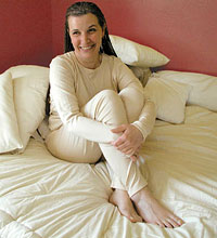 woman dressed in organic cotton long johns sitting in bed made up with organic sheets